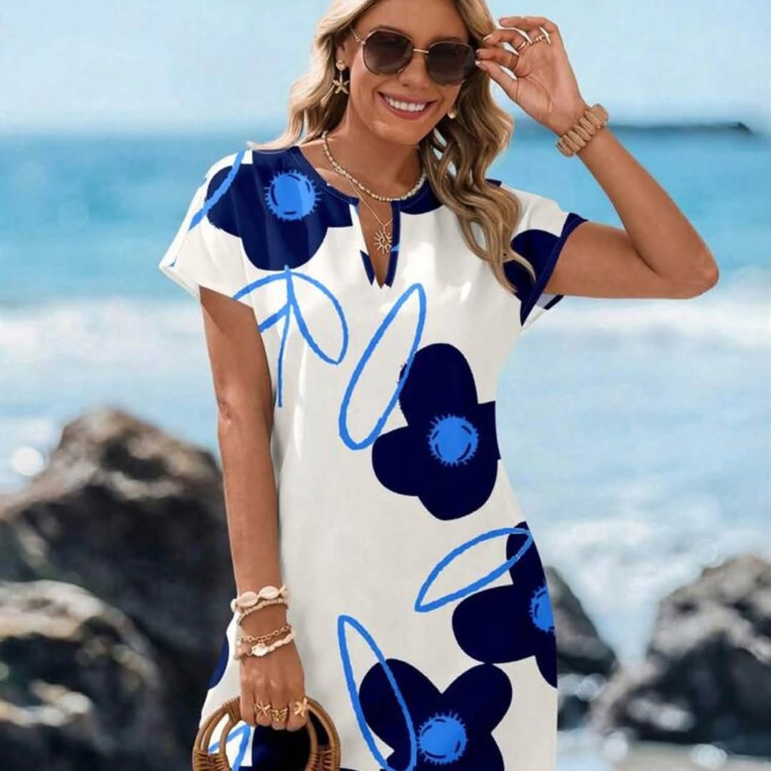 Femme souriante en robe blanche à grandes fleurs bleues, au bord de la mer